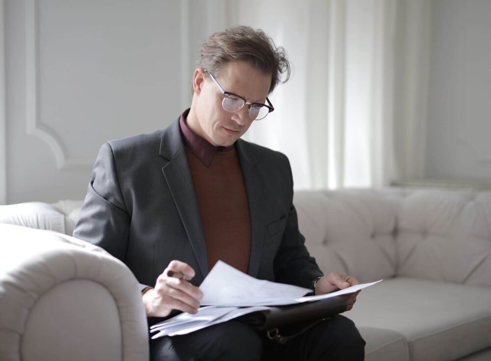 Man reading through documents on a sofa.