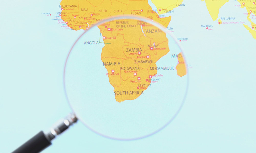 A world map with a magnifying glass highlighting the continent of Africa, focusing on the southern region.