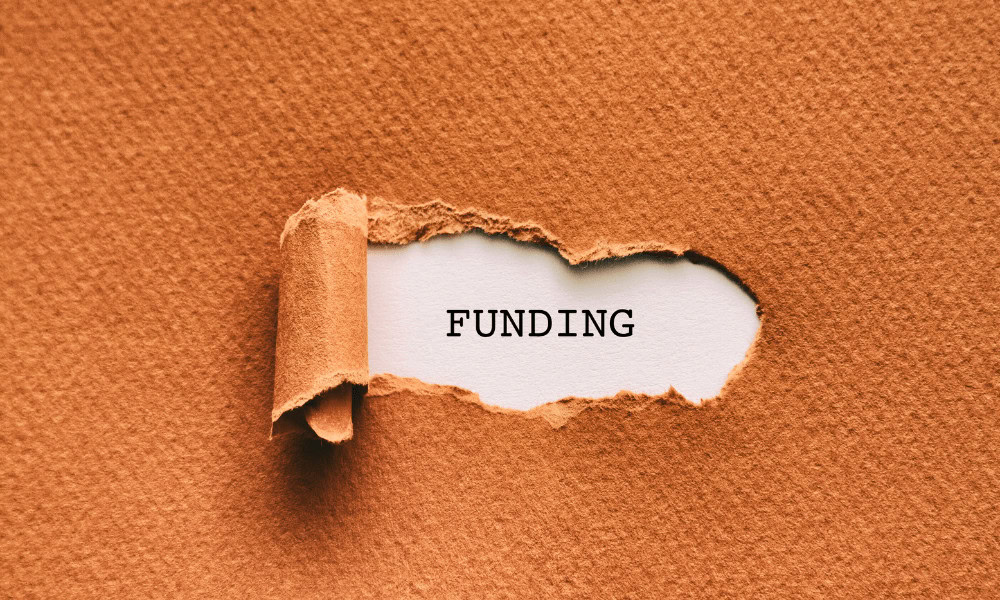 A piece of brown cardboard paper that has been peeled back to reveal the word funding.